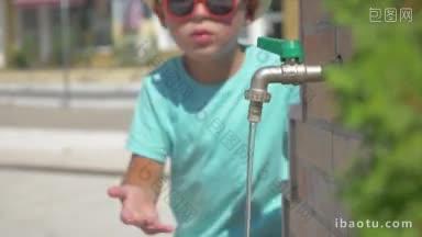 戴着草帽和太阳眼镜的男孩在公共<strong>场合</strong>在喷泉水龙头边洗手、洗澡