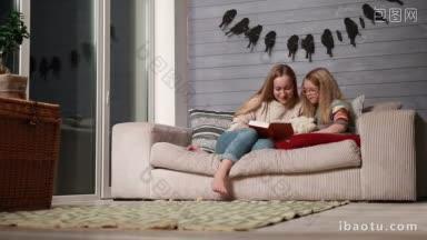 年轻漂亮的妈妈和可爱的小女儿舒服地坐在家里的沙发上，一起读一<strong>本</strong>有趣的书