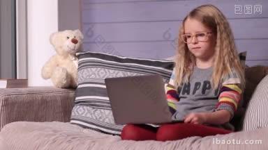 微笑的小<strong>女孩</strong>与笔记本电脑坐在家里舒适的沙发上和她的朋友网上聊天的小孩