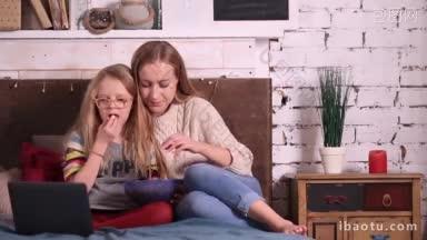 迷人的妈妈和她美丽的十几岁的女孩坐在卧室里，在现代便携式电脑上看<strong>卡通片</strong>家庭享受