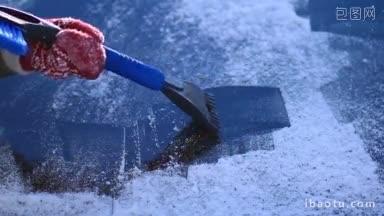戴着红色羊毛手套的女人用塑料冰刮汽<strong>车</strong>前挡风玻璃上的冰和雪