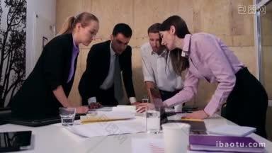 四位<strong>业务</strong>同事站在桌子周围分析和计划，低头看蓝图