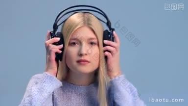 漂亮的女孩听音乐的耳机在一个白色的<strong>背景</strong>，看着相机近距离的年轻金发