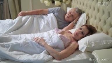 美丽的老妇人在床上醒来，伸懒腰，而她的丈夫还在睡觉，可爱的成熟女士醒来