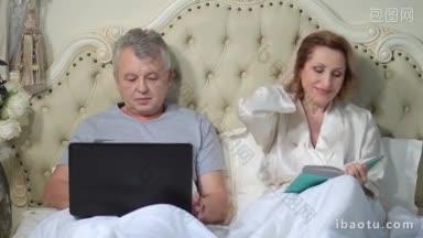 面带微笑的老夫妇在床上放松着笔记本电脑和书，放松的老夫妇躺在家庭床上