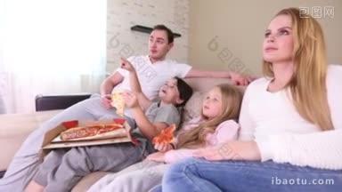年轻的父母和他们的孩子坐在家里的沙发上看电视，吃着披萨，<strong>微笑</strong>着