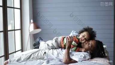 快乐英俊的留着脏辫的非裔美国父亲躺在床上和快乐的蹒跚学步的儿子玩耍你是我的世界!