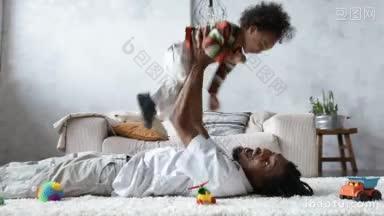 侧面的俏皮的非裔美<strong>国父</strong>亲举起卷曲的混合种族蹒跚学步的儿子，而躺在家里的地板上