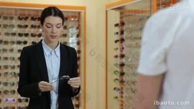 迷人的女眼科医生在眼镜店眼镜陈列柜前向年轻的男病人展示眼镜