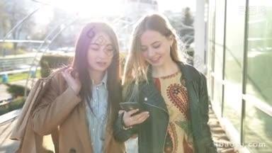 两个迷人的多民族女孩带着<strong>购物</strong>袋走在城市街道上使用智能手机，<strong>购物</strong>后在辉光