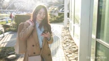 优雅的亚洲年轻女子肩上背着购物袋，在城市的街道上用手机上网