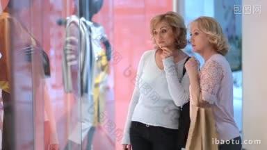 快乐的高级女朋友拿着购物袋站在<strong>商店</strong>橱窗旁边，看着商场里迷离的衣服