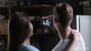 背面正面的年轻夫妇站在一起拥抱和用手机在家庭厨房自画像集中在形象