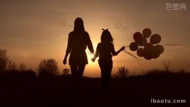 年轻的母亲和她可爱的小女儿手牵彩色气球走在草地上的剪影