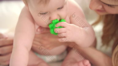 婴儿坐着妈妈。拥抱婴儿尿布吃绿色玩具