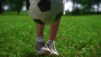 特写镜头孩子脚踢足球球男孩玩绿色草坪上公园