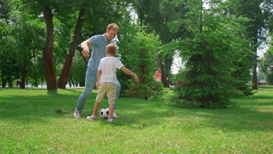 快乐父亲教学儿子玩足球快乐的男孩通过球爸爸草坪上