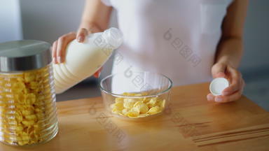 女人手倒牛奶玻璃碗玉米片准备早餐