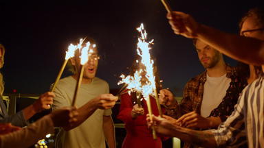 多民族朋友享受生日聚会，派对屋顶人燃烧罗马焰火筒