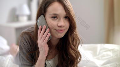年轻的女人会说话的移动电话床上微笑女人会说话的电话