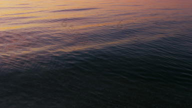 特写镜头平静海洋水表面反映明亮的粉红色的日出天空早....