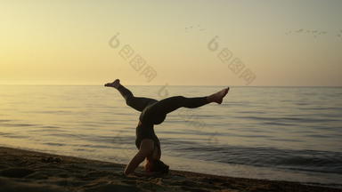 苗条的女孩保持平衡头<strong>手倒立</strong>在户外瑜伽女人培训海滩