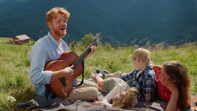父亲玩吉他自然快乐家庭唱歌坐着毯子野餐