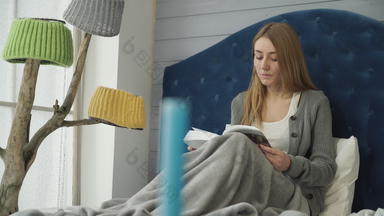 年轻的女孩阅读书坐着床上