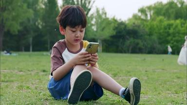 男孩坐在草地上看手机学龄前户外宣传视频