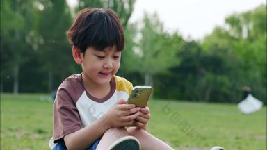 男孩坐在草地上看手机休闲装素材