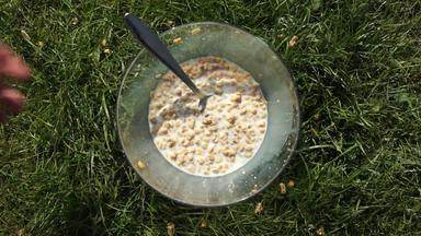 早餐准备好了男人。手把牛奶什锦早餐危机格兰诺拉麦片谷物填满牛奶透明的碗绿色草草坪上表格前拍摄
