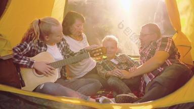 旅游家庭休息玩吉他音乐内部野营帐篷阳光明媚的森林笑家庭唱歌首歌吉他旅游帐篷营地快乐家庭森林徒步旅行假期