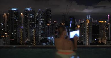 视图女人采取笔记平板电脑游泳池摩天大楼屋顶晚上城市景观(泥<strong>马来西亚</strong>
