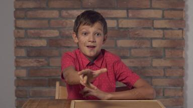 孩子坐着桌子上持有白板纸上的内容刻字飞背景红色的砖墙