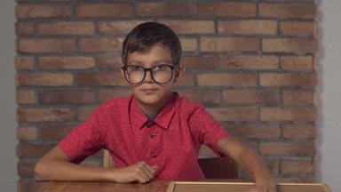 孩子坐着桌子上持有白板纸上的内容刻字银行背景红色的砖墙