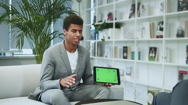 黑色的正式的男人。使演讲平板电脑绿色色度屏幕年轻的非裔美国人男人。西装坐着办公室沙发匿名的同事使演讲平板电脑