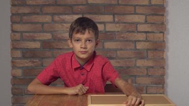 孩子坐着桌子上持有白板纸上的内容刻字老板背景红色的砖墙