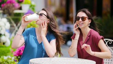年轻的女孩聪明的电话在户外咖啡馆女性购物袋坐着露天咖啡馆咖啡智能手机