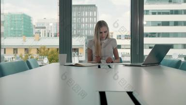 年轻的业务女人会议房间论文优雅的金发碧眼的女人坐着长表格现代大厅办公室移动PC写作论文工作