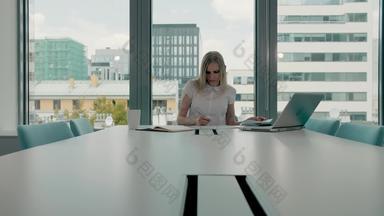 年轻的女商人会议房间论文优雅的金发碧眼的女人坐着长表格现代大厅办公室移动PC写作论文工作