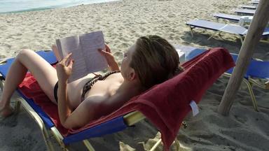 年轻的青少年阅读书海滩稳定摄像头起重机拍摄