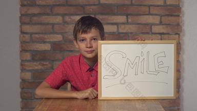 孩子坐着桌子上持有<strong>白板</strong>纸上的内容刻字微笑背景红色的砖墙