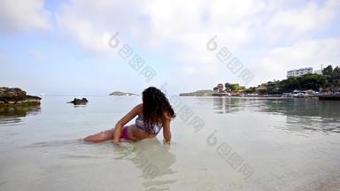 漂亮的女坐着夏天海滩浅水让人耳目一新溅水平移拍摄