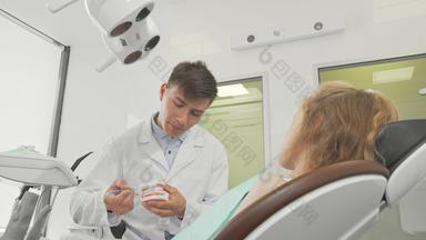 年轻的男性牙医显示刷牙齿牙科模型