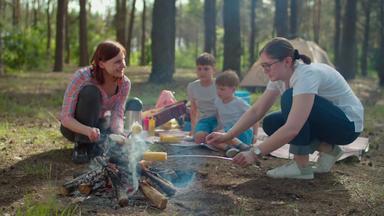 母亲烹饪香肠玉米火儿子坐着野餐毯子夏天家庭野营假期帐篷森林慢运动<strong>替身</strong>拍摄