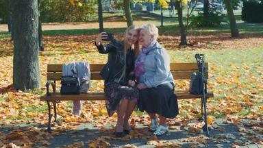 变焦拍摄年轻的<strong>女性</strong>使自拍智能<strong>手机</strong>秋天时间美丽的公园