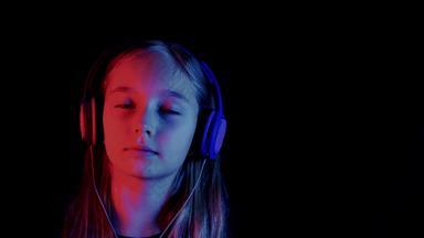 美丽的少年女孩听音乐耳机黑暗房间霓虹灯照明放松女孩享受音乐耳机黑色的工作室红色的蓝色的照明