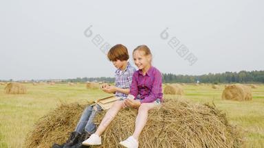 少年男孩女孩坐着干草堆农村场无忧无虑的男孩女孩阅读书有堆栈收获场青少年支出假期村