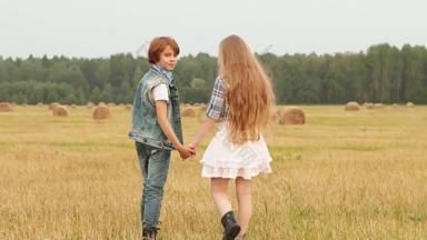 少年夫妇持有手走农村场干草堆背景浪漫的女孩男孩把收获场年轻的夫妇摆姿势农村场