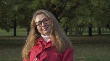 肖像年轻的微笑女人眼镜红色的夹克绿色公园媒介拍摄慢运动